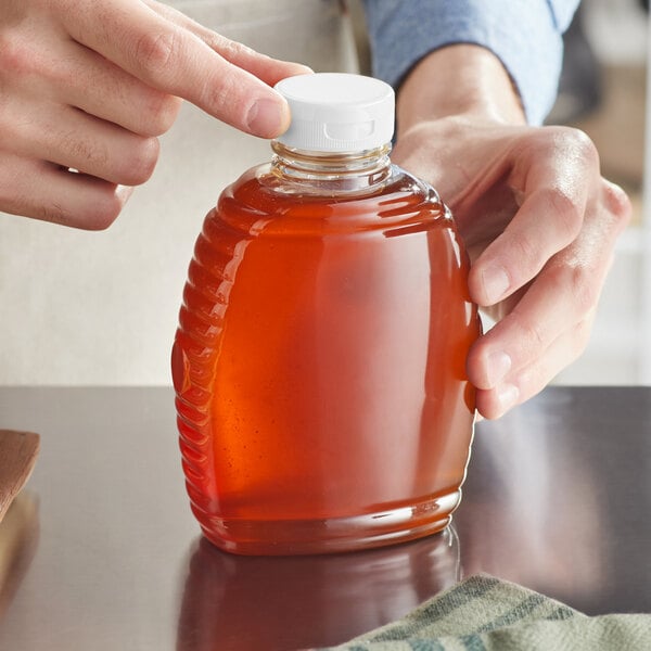 A hand pouring honey into a Queenline PET honey bottle on a counter.