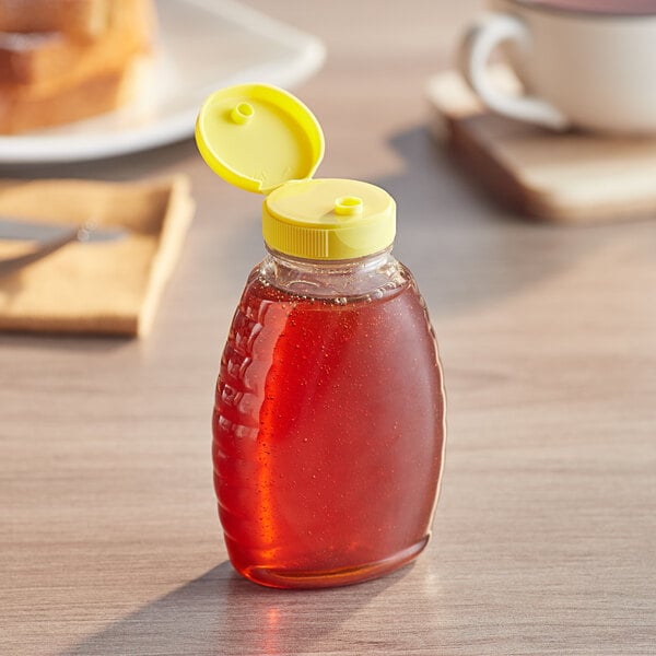 A Classic Queenline PET honey bottle with a yellow plastic flip top lid on a table.