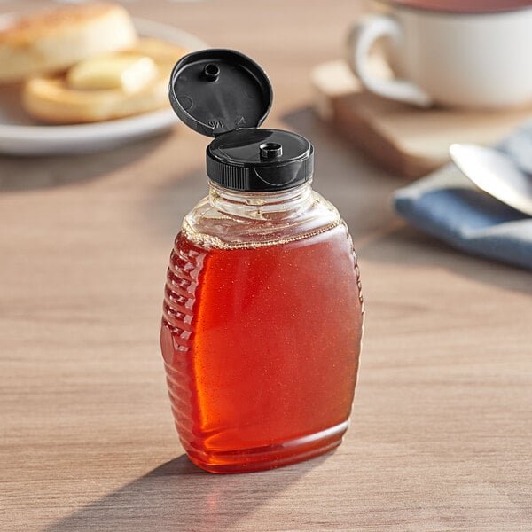 An 8 oz. Queenline PET honey bottle with a black flip top lid on a table.