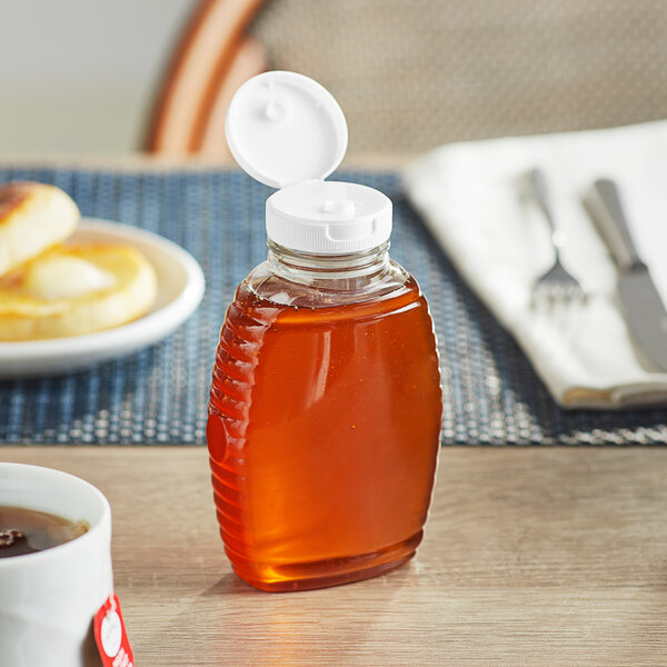 An 8 oz. Queenline PET honey bottle with a white flip top lid on a table next to a cup of coffee.