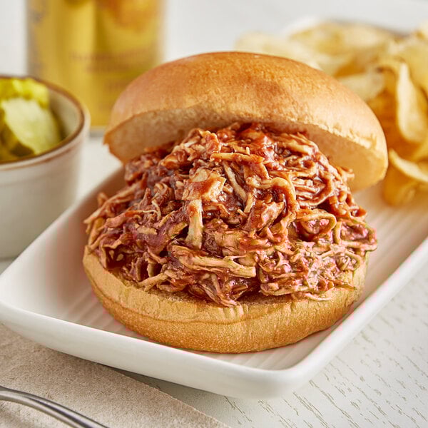 A pulled pork sandwich with Ray's No Sugar Added Barbecue Sauce on a white plate with chips.