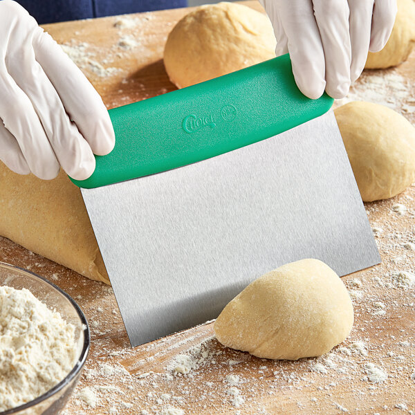 A person in gloves using a Choice stainless steel dough cutter with a green handle to cut dough on a cutting board.