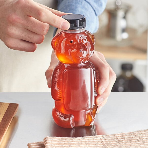 A person pouring honey into a bear shaped PET honey bottle on a wooden counter.