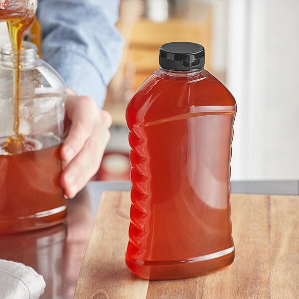 A hand pouring honey into a ribbed hourglass honey bottle on a table.