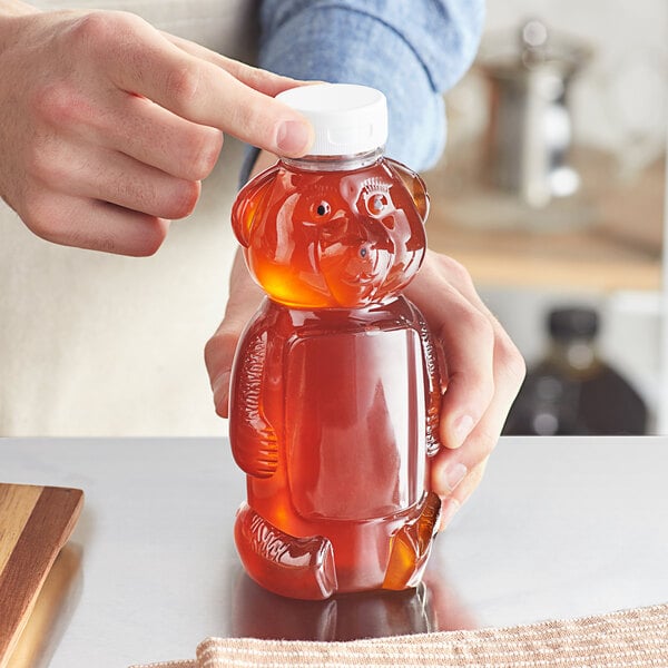 A person pouring honey into a bear-shaped PET bottle with a flip top lid.