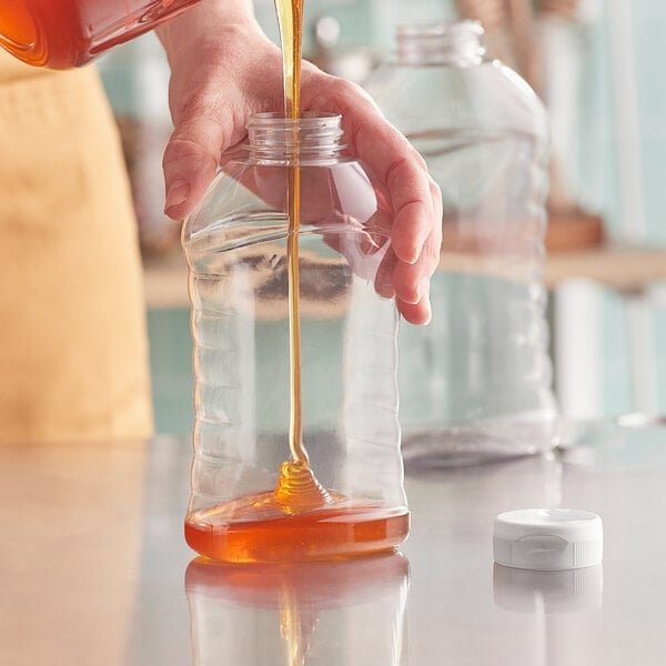 A person pouring honey into a ribbed plastic bottle.