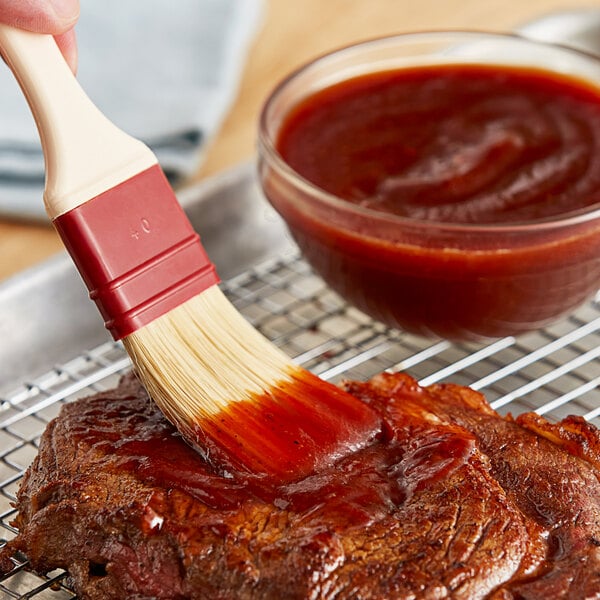 A person using a brush to spread Sweet Baby Ray's Original BBQ Sauce on a steak.
