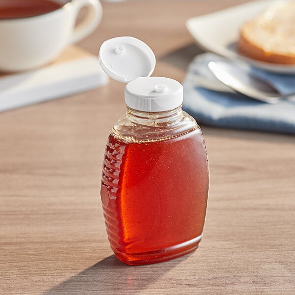 A Queenline PET honey bottle with a white plastic flip top lid on a table next to a cup of tea.