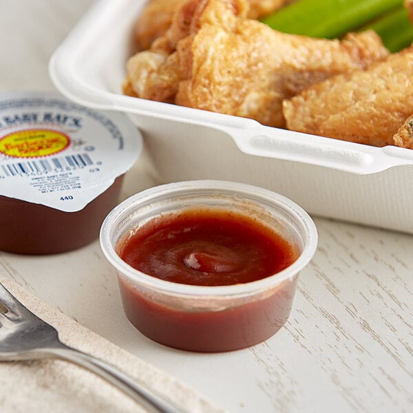 A white container of chicken wings with a plastic cup of Sweet Baby Ray's Original BBQ Sauce.