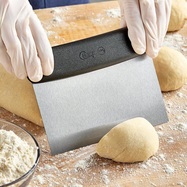 A person using a Choice stainless steel dough cutter with a black handle to cut dough on a counter.