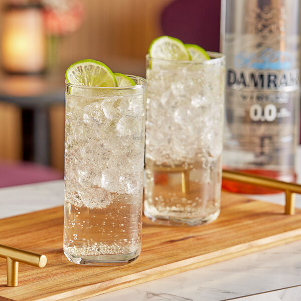 Two glasses of Damrak Virgin Non-Alcoholic Gin with lime and ice on a wooden tray.