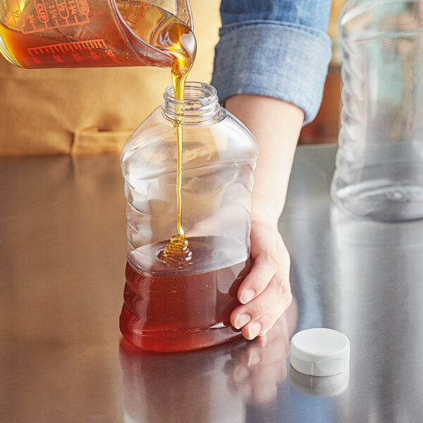 A person pouring honey into a Ribbed Hourglass PET Honey Bottle.