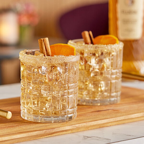 Two glasses of Fluere Non-Alcoholic Spiced Cane Rum with ice and orange slices on a table.