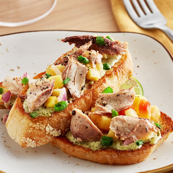 A plate with Sea Tales Mackerel Fillets in oil, bread, and vegetables with a fork and knife.