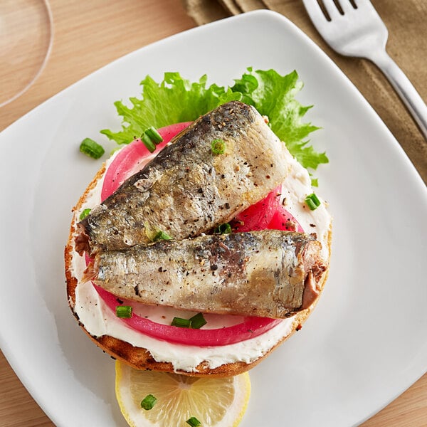 A plate with a fish sandwich and a lemon slice on a table.
