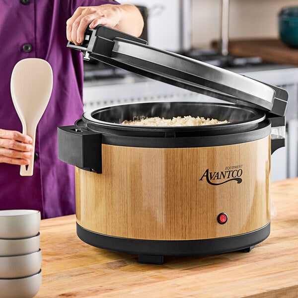 A woman using an Avantco woodgrain electric rice warmer in a home kitchen.