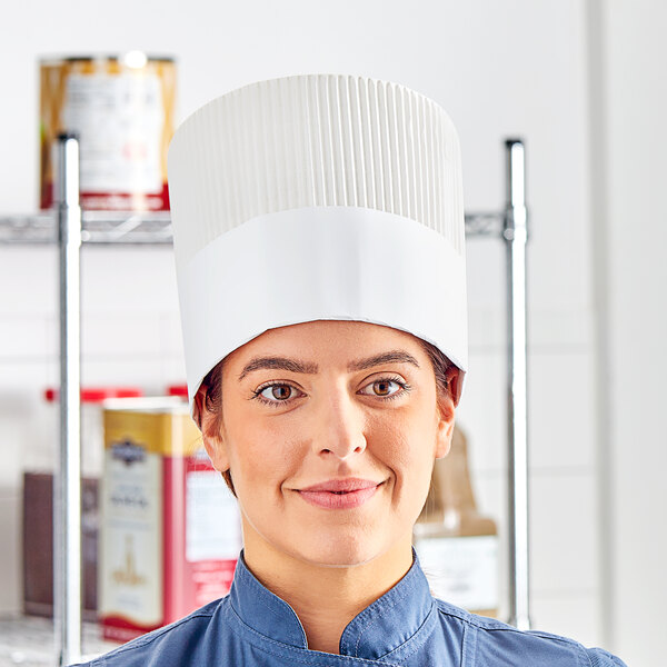 A woman wearing a white fully formed disposable chef hat.