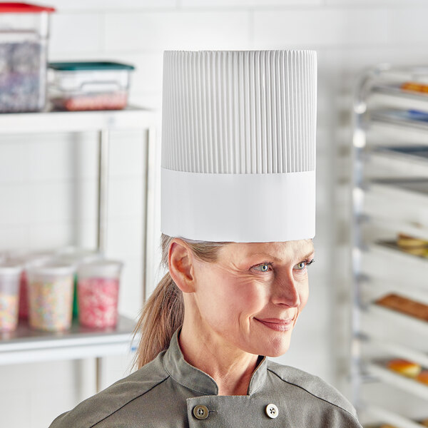 A woman wearing a Choice white disposable chef hat in a professional kitchen.