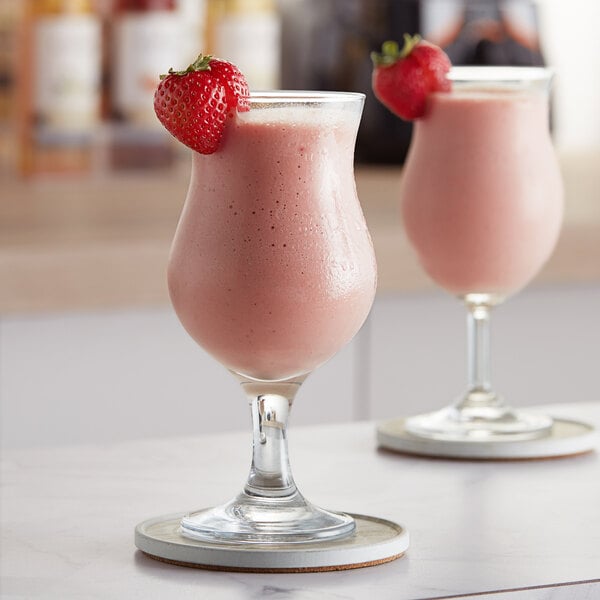 Two glasses of pink strawberry smoothie with a strawberry on top.