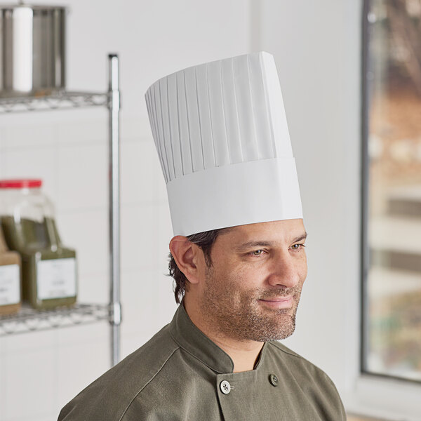 A man in a white pleated Choice chef hat on a counter in a professional kitchen.