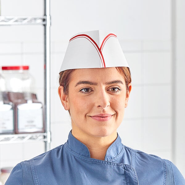 A woman wearing a Choice red striped disposable chef hat at a professional kitchen counter.