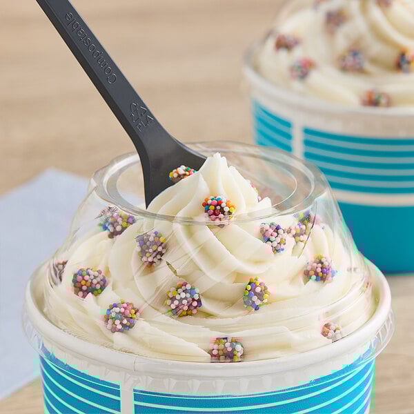 A clear plastic dome lid with a hole on a cup of ice cream with sprinkles and a spoon.