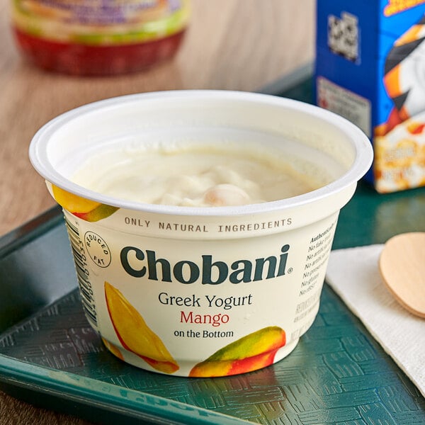 A white container of Chobani Low-Fat Mango Greek Yogurt on a table with a spoon on top.