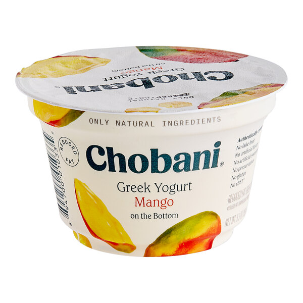 A case of 12 Chobani Low-Fat Mango Greek Yogurt cups on a table in a corporate cafeteria.