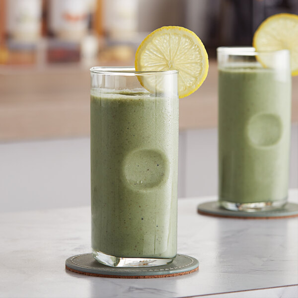 Two glasses of green liquid with lemon slices on them.