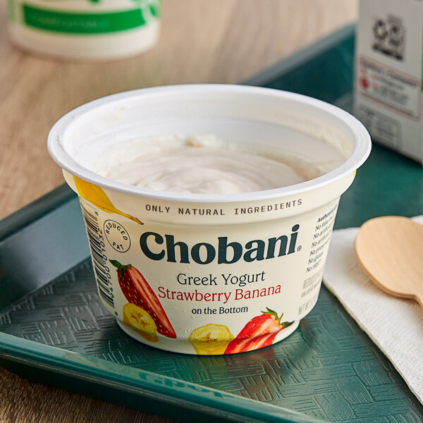 A white and green Chobani Low-Fat Strawberry Banana Greek Yogurt container with a wooden spoon on top.