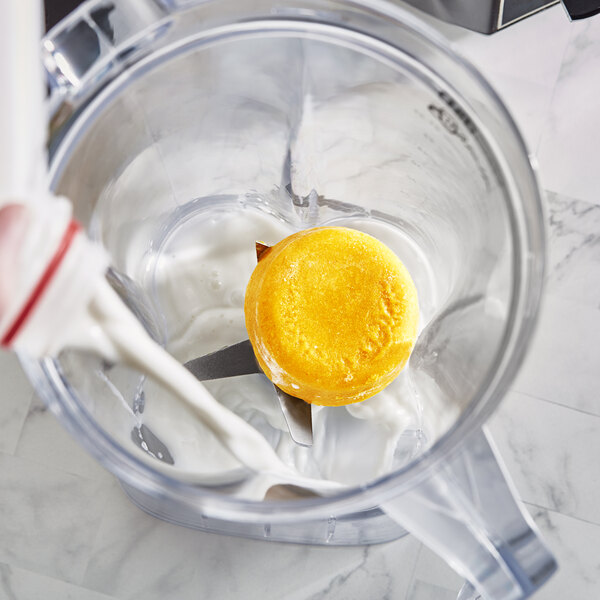 A blender with yellow frozen smoothie pucks in it.