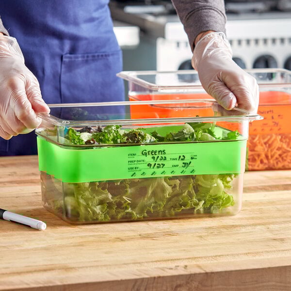 A person wearing gloves writes on a plastic container of lettuce using a Choice Green Write-On Food Pan Band.