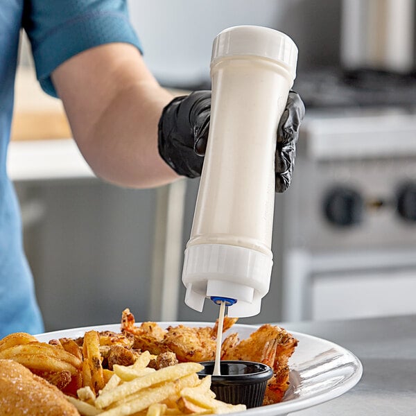 A person using a San Jamar sauce bottle to pour sauce onto a plate of fried food.