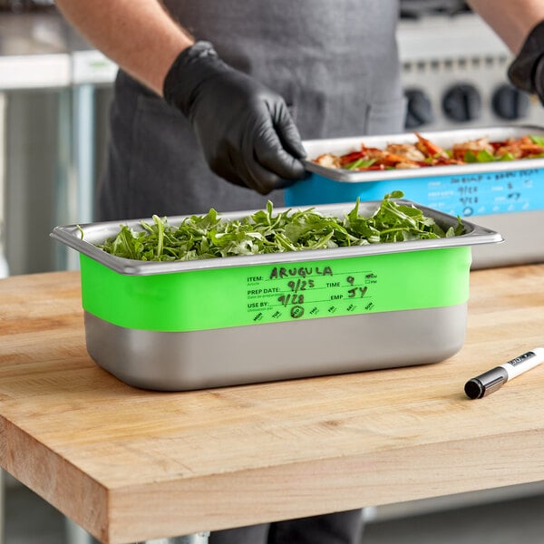 A person wearing black gloves writes on a blue Vigor Green food container.