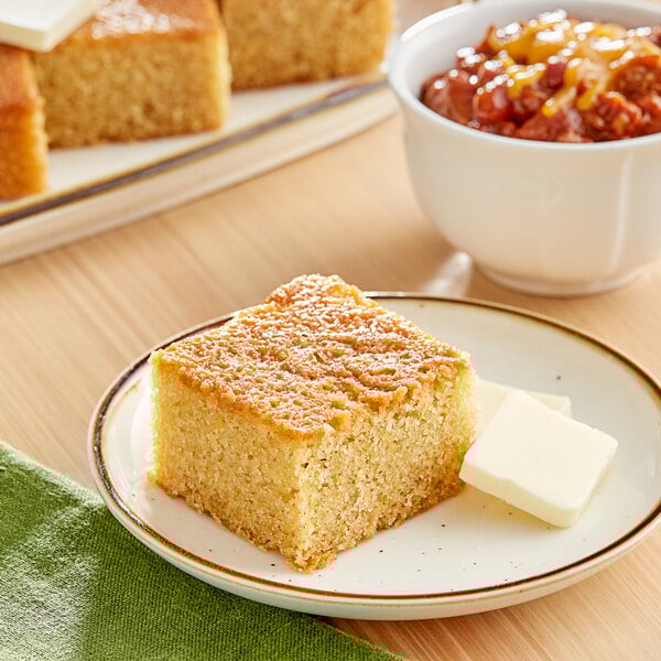 A plate of Abe's vegan cornbread with butter on a table with a bowl of chili.