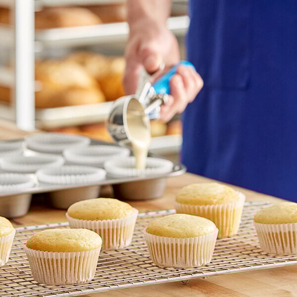 Muffins sit on a wire cooling rack. A person is pouring muffin batter into a muffin tin in the background.