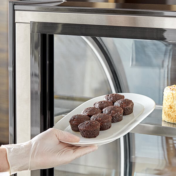 A gloved hand placing a plate of Abe's vegan chocolate brownies into a pastry case.