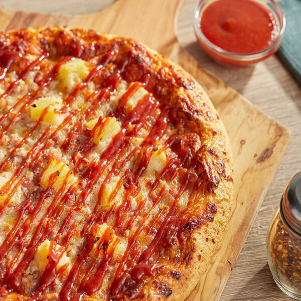 A pizza with Cattlemen's Hawaiian Tangy Sweet BBQ Sauce and pineapple on a wooden board.