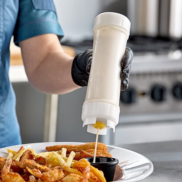 A person using a San Jamar sauce bottle to pour sauce onto a plate of fries.