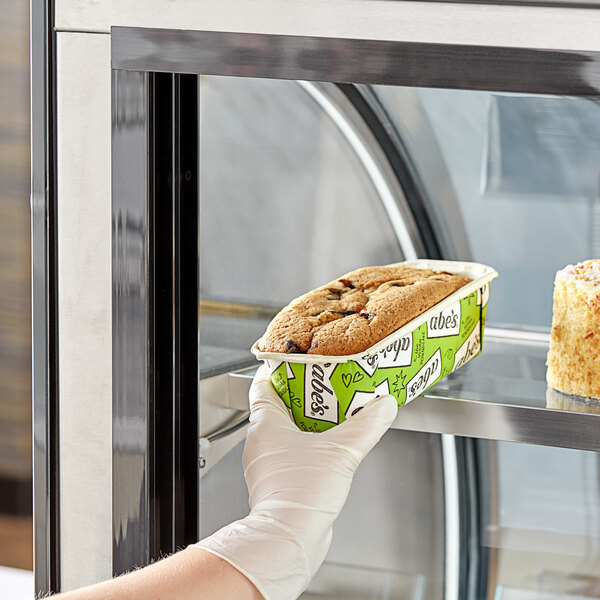 A gloved hand placing a container of Abe's vegan blueberry pound cake into a pastry case.