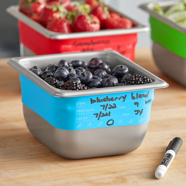 A Vigor Blue stainless steel food pan with a bowl of blueberries and blackberries and a pen on the counter.