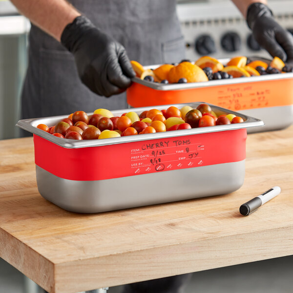 A man using Vigor Write-On Food Pan Bands to label two stainless steel food pans on a table.