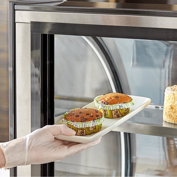 A gloved hand placing a plate of chocolate muffins into a pastry case.