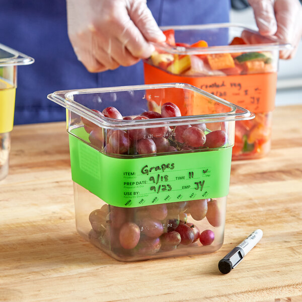A white pen with a black tip writing "grapes" on a yellow plastic container of grapes.