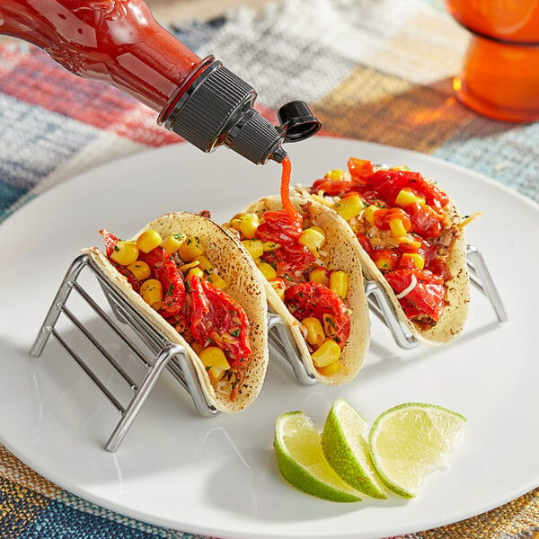 A plate of tacos with a bottle of Frank's RedHot Sriracha Chili Sauce on the table.