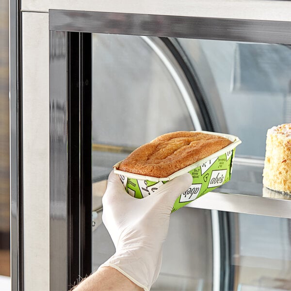 A gloved hand placing a container of Abe's vegan vanilla pound cake into a pastry case.