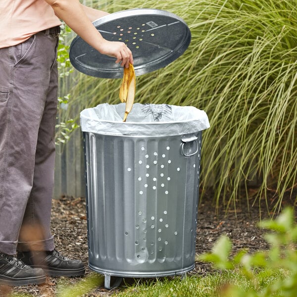 A person using a Behrens galvanized steel compost bin with a lid to throw away a banana.