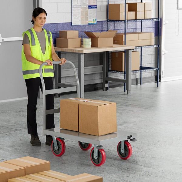 A woman in a yellow reflective vest pushing a Lavex Pro heavy-duty steel platform truck with boxes.