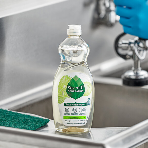 A person wearing blue gloves using Seventh Generation dish soap to clean a stainless steel sink.