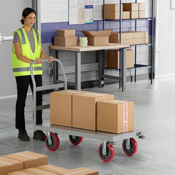 A woman in a reflective vest pushing a Lavex Pro steel platform truck with cardboard boxes on it.